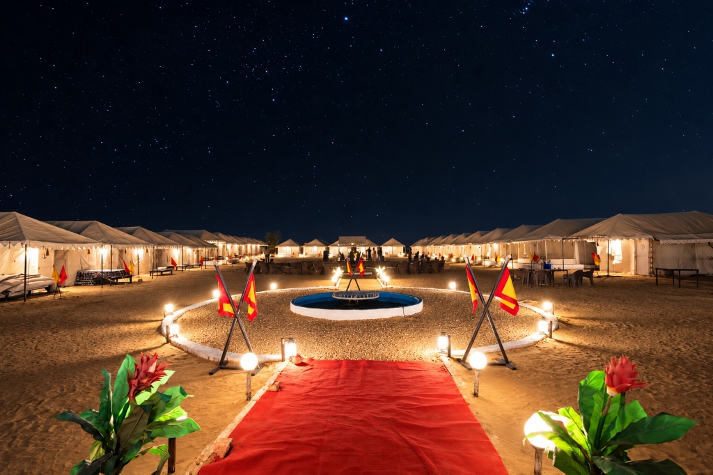 Panoramic starlit night sky over RETIVAA Desert Camp luxury desert camp with illuminated tents and red carpet pathway